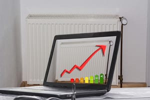 Vooraanzicht van een radiator voor een lichtgekleurde muur met open laptop en energie-efficiëntiediagram met rode pijl