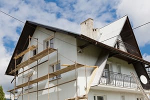 Einfamilienhaus leicht seitlich frontal mit weißer Putzfassade Gerüst und Giebelbalkon unter Blechdach