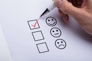 Close-up van hand met pen die een rood vinkje plaatst in het bovenste vakje van een smileywaarderingsblad van bovenaf