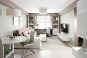 Lichte woon-/eetkamer in modern appartement vanuit het perspectief van de voorkant met een bank, eettafel, tv-scherm en werkplek bij het raam