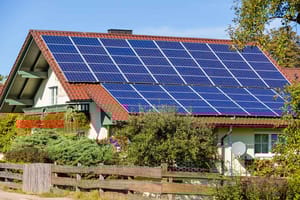 Vooraanzicht van een vrijstaand huis met schuin dak en grote zonnepanelen Balkon met bloemen en tuinhek