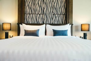 Blick auf Schlafzimmer mit großem Doppelbett, zwei Zierkissen, Nachttischen und dekorativem Wandpaneel