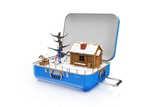 Schräg von oben auf Miniaturholzblockhütte in offenem blauem Koffer mit Schnee, Schneemann, kahlem Baum und Brunnen