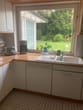 Vista para uma cozinha moderna embutida com lava-loiças, máquina de lavar loiça e bancada em frente a uma grande janela com vista para o jardim