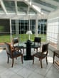 Varanda de Inverno com telhado de vidro e caixilharia branca com mesa redonda de vidro com quatro cadeiras de couro e vista para o jardim
