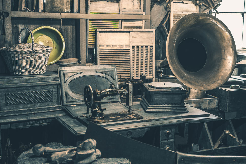 Innenansicht eines Dachbodens mit sichtbarer Holzbalkendecke antiken Möbeln Nähmaschine und Grammophon frontal