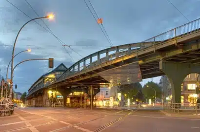 Straßenblick unter erhöhter Stahl-U-Bahntrasse bei Dämmerung aus unterer Perspektive markante Bögen