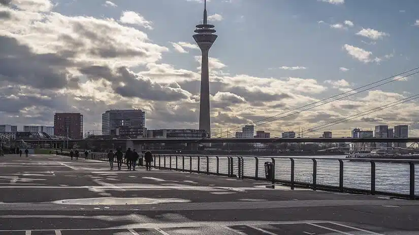 Seitlicher Blick auf Rheinuferpromenade mit Fernsehturm und Büro- und Wohnhochhäusern im Hintergrund