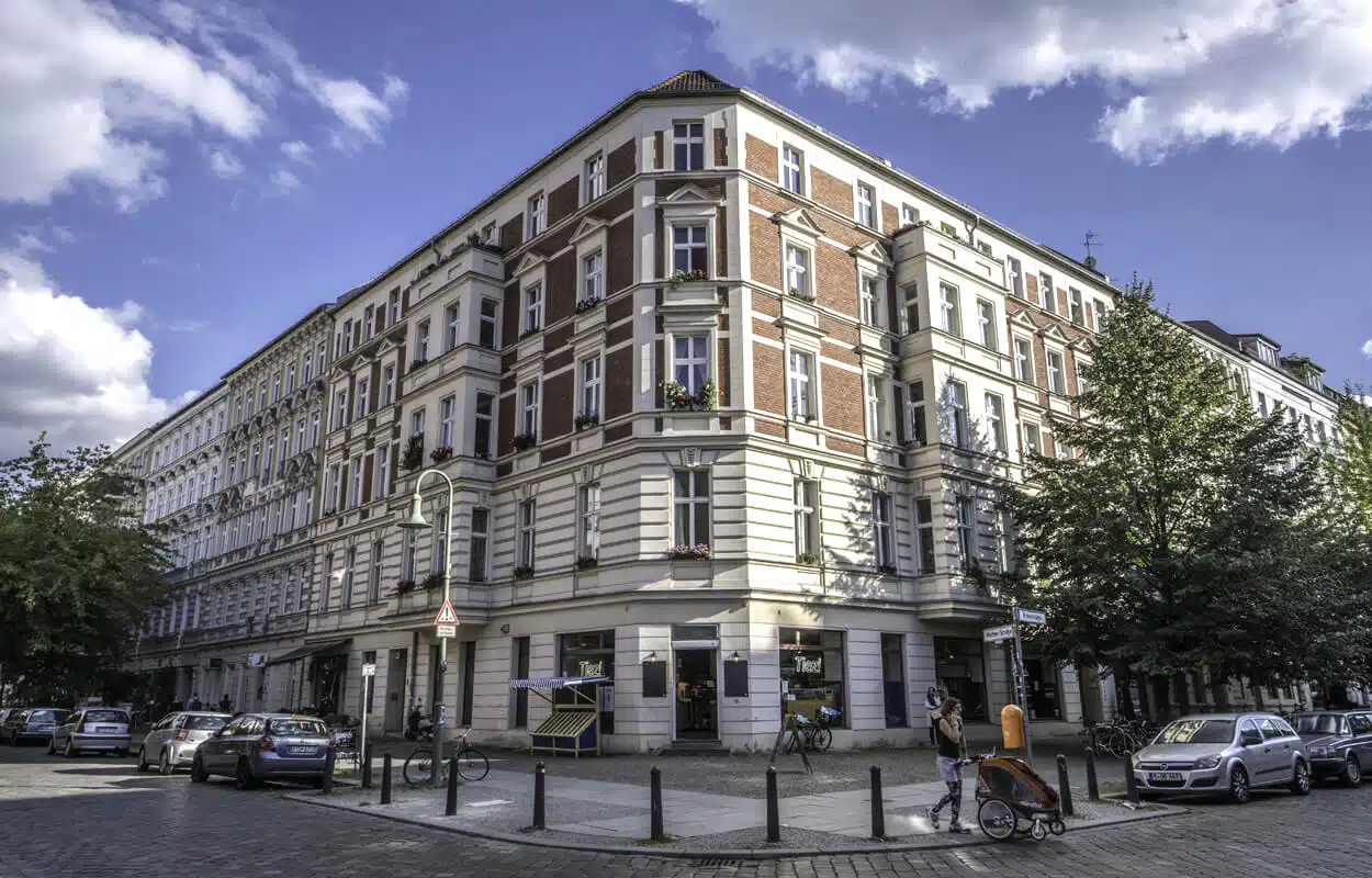 Eckaltbau mit roter Klinker- und weißer Putzfassade aus Straßenperspektive mit Fensterblumenkästen und Erdgeschossgeschäft