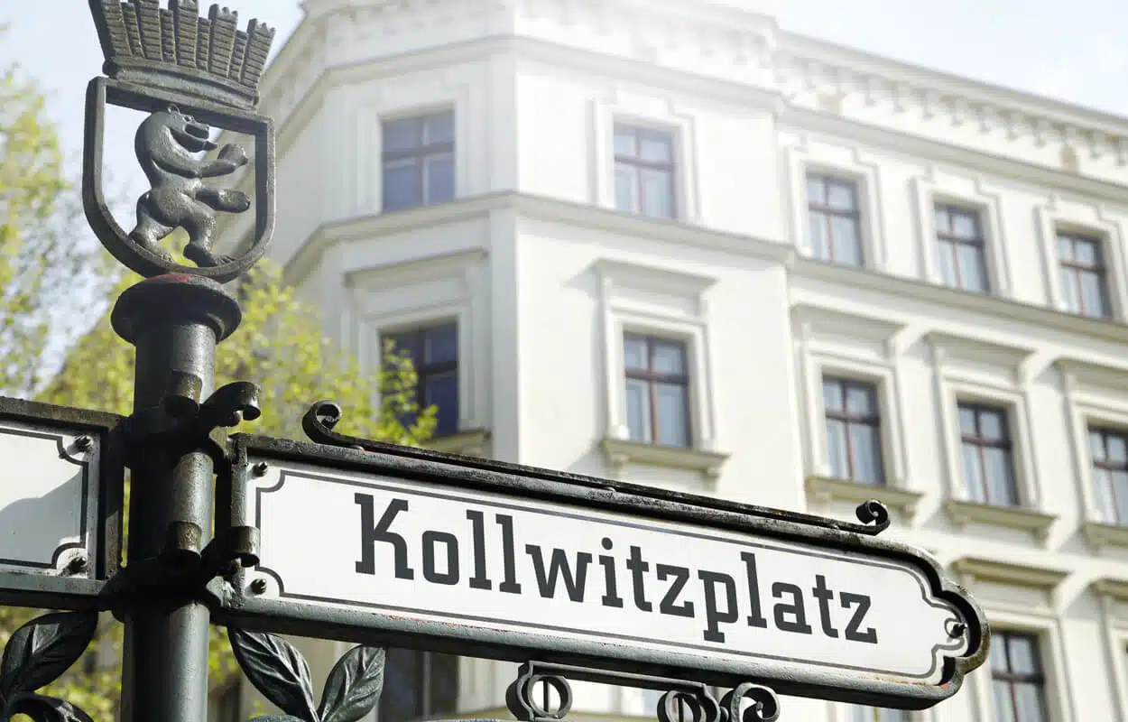 Berliner Eckhaus im Altbau mit weißer Putzfassade und dunklen Sprossenfenstern aus Straßenperspektive am Kollwitzplatz