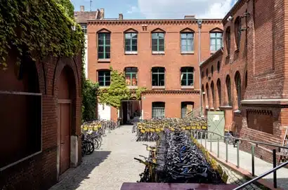 Blick in den Innenhof eines roten Klinkergebäudes mit zahlreichen Fahrrädern und efeubewachsenen Mauern