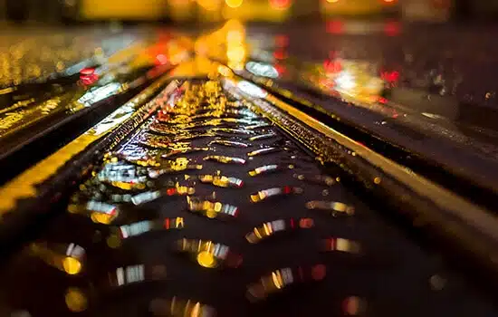 nasse Straßenbahnschienen bei Nacht aus Froschperspektive mit bunten Lichtreflexionen