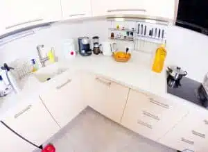 weiße Küchenzeile in V-Form aus Vogelperspektive mit Spüle, Kochfeld, Kaffeemaschine und Obstkorb