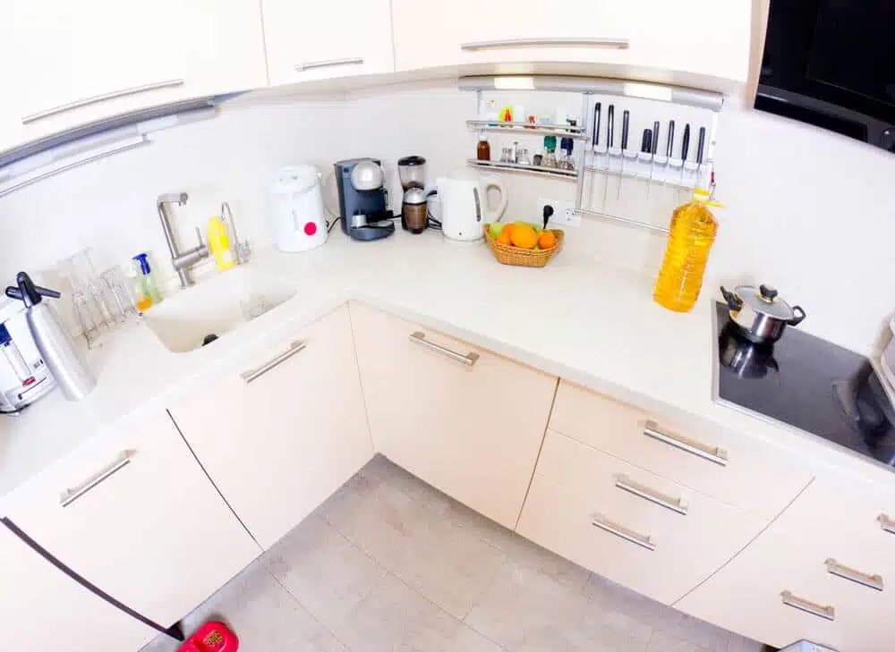 weiße Küchenzeile in V-Form aus Vogelperspektive mit Spüle, Kochfeld, Kaffeemaschine und Obstkorb