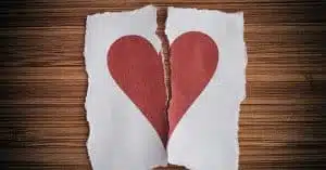 zerrissenes rotes Herz auf zwei Papierfetzen vor hölzernem Hintergrund