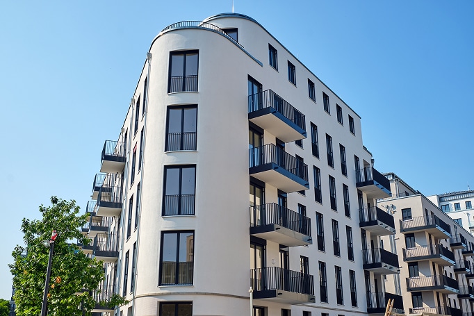Eckansicht modernes Mehrfamilienhaus mit geschwungener Fassade und schwarzen Balkonen aus bodentiefen Fenstern