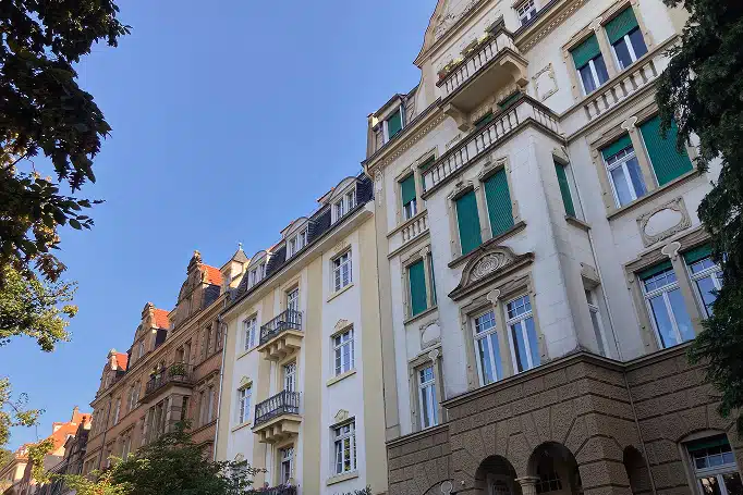 Froschperspektive auf historische Mehrfamilienhäuser mit Balkonen und grünen Fensterläden