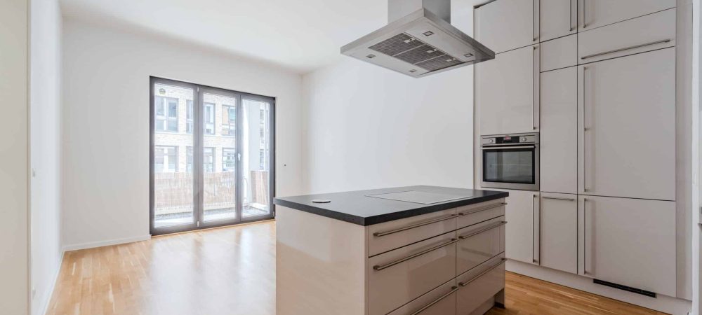 Offener Wohn- und Küchenbereich mit Kochinsel, Edelstahl-Dunstabzug, Einbauküche und bodentiefen Glasschiebetüren zum Balkon