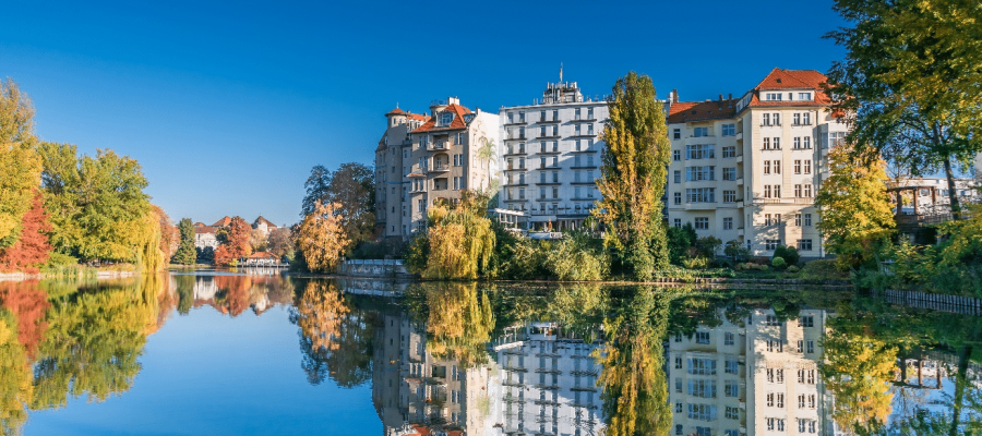 Blick auf mehrgeschossige Uferhäuser mit roten Dachziegeln und Balkonen spiegelnd im ruhigen See